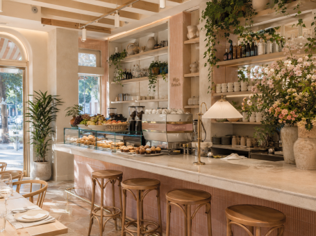 Barra de cafetería de brunch en Madrid Barra de cafetería de brunch en Madrid con exposición de bollería, taburetes de madera, flores y decoración cálida.
