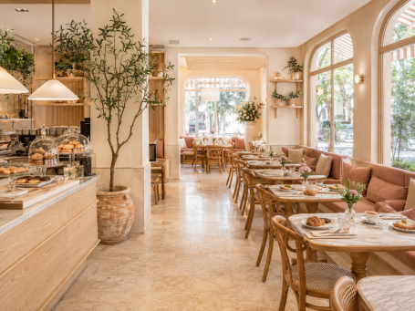 Salón de cafetería de brunch en Madrid Salón de cafetería de brunch en Madrid con mesas de madera, bancos tapizados en rosa y ambiente luminoso y acogedor.