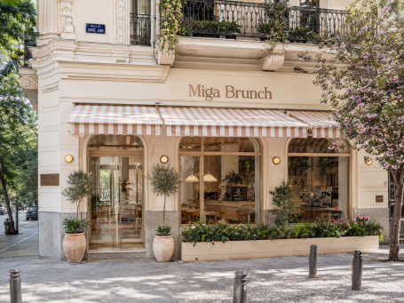Fachada de cafetería de brunch en Madrid Fachada de cafetería de brunch en Madrid con toldos a rayas, grandes ventanales y diseño exterior elegante y luminoso.